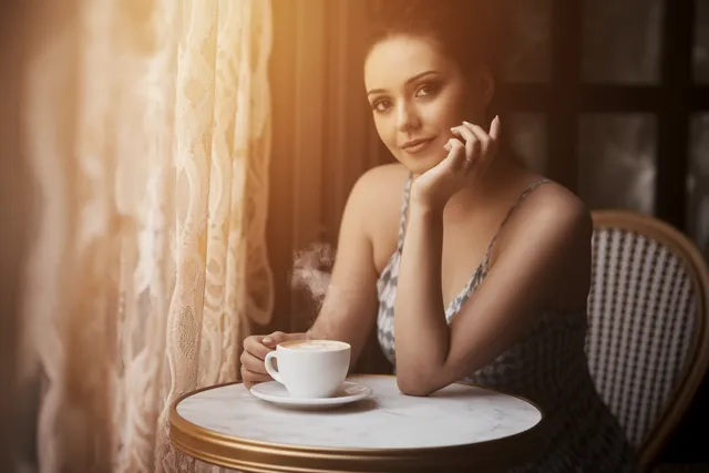 A portrait photo of a woman sitting with a flat white coffee in a Parisienne cafe